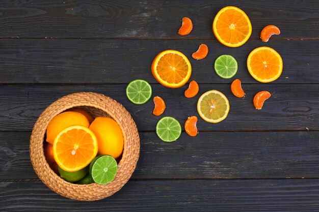 Bowl of citrus fruits on black wooden, top view