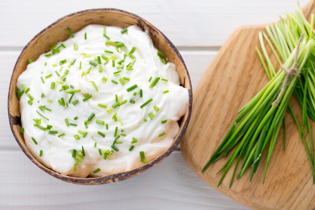 Bowl of cream cheese with green onions, dip sauce on wooden table.