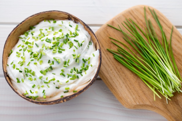 Bowl of cream cheese with green onions, dip sauce on wooden table.