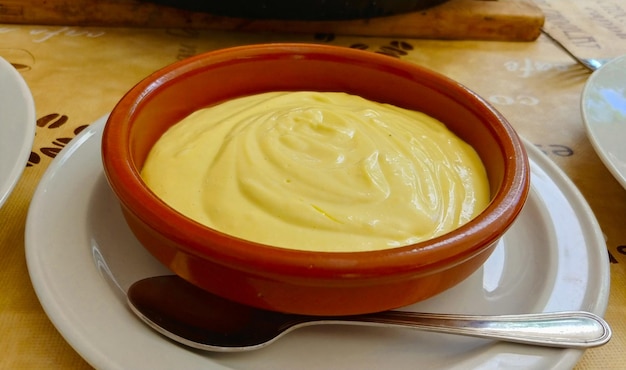 A bowl of creamy mayonnaise sits on a plate with a spoon.