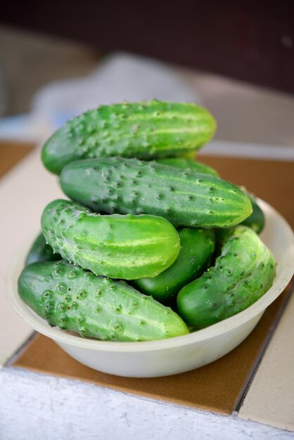 A bowl of cucumbers sits on a table with a silver and brown trim.