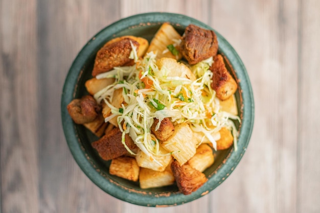 Чаша вкусной традиционной уличной еды Yuca Con Chicharron на деревянном столе в Гондурасе