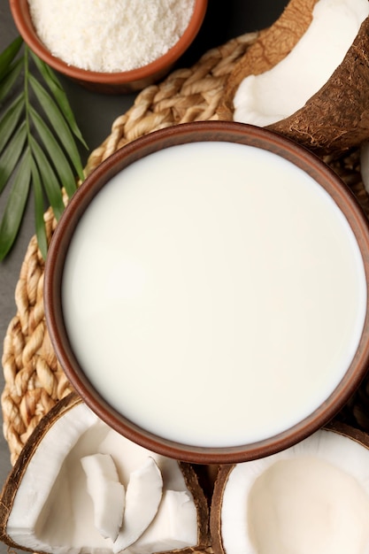 Bowl of delicious vegan milk near coconut pieces on grey table flat lay