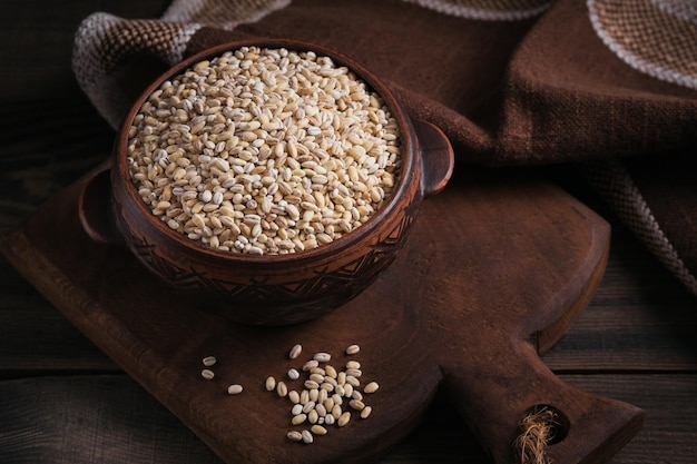 Bowl of dry raw broken pearl barley cereal grain on dark wooden background Cooking pearl barley porridge concept