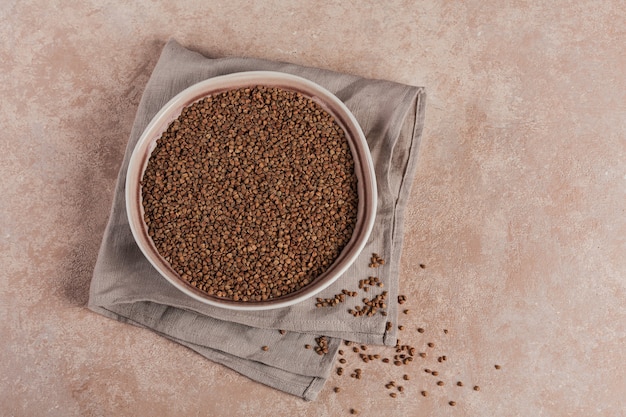 Bowl of dry raw buckwheat groats on light beige background