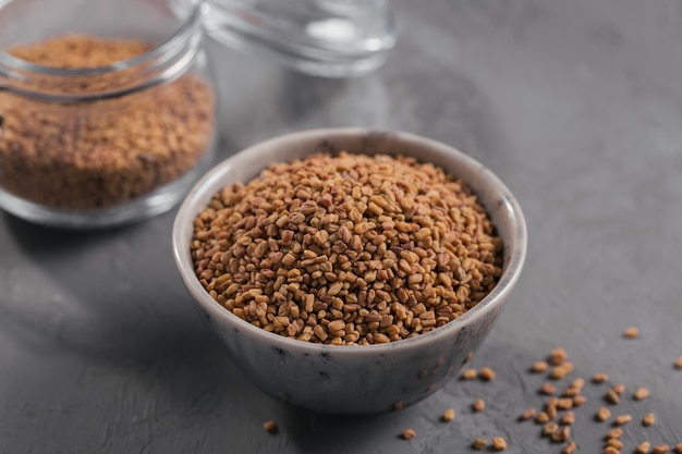 Bowl of fenugreek dry seeds on grey background. Healthy food, Ayurveda and alternative medicine concept