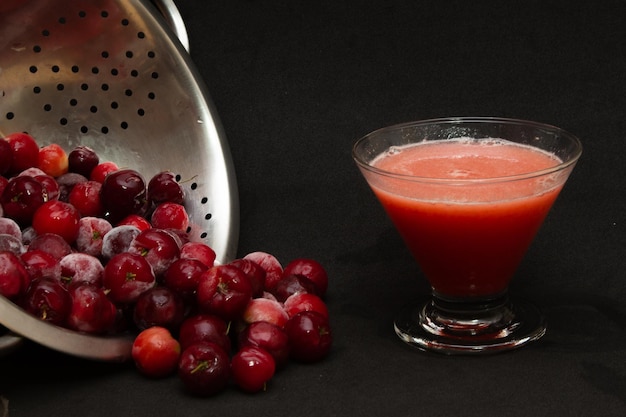 Bowl filled with fresh acerolas next to acerola juice