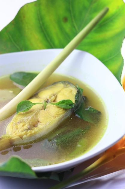 A bowl of fish soup with a green leaf on the side.