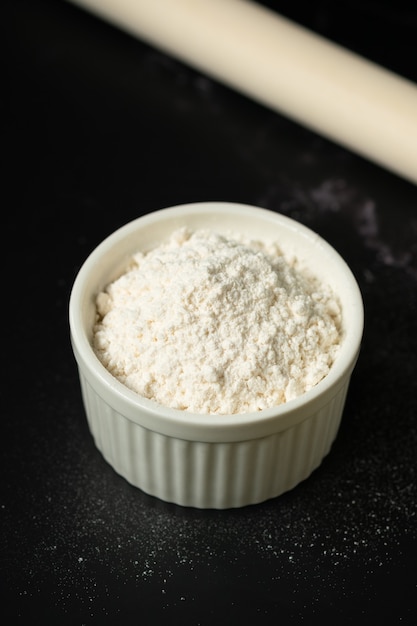 Bowl of flour on dark surface.Flour in ceramic cup.Starch cup with copy space.