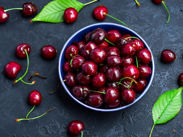 bowl of fresh cherry with leaves on a dark background