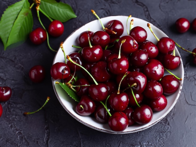 bowl of fresh cherry with leaves on a dark background