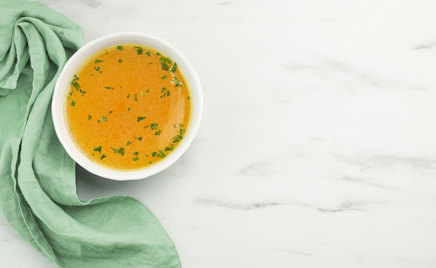 Bowl of fresh chicken broth on light kitchen table, top view