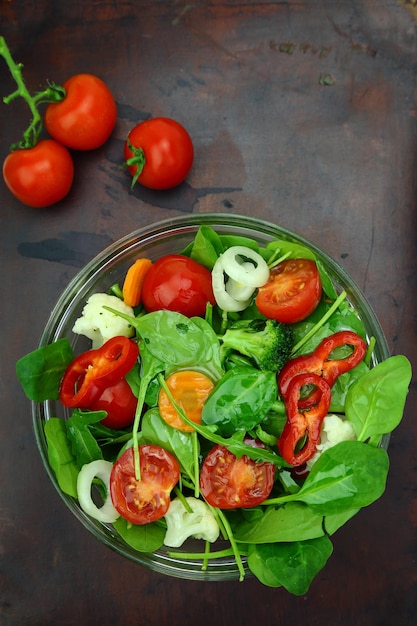 Bowl of fresh colorful salad and tomato cherries on wooden surface