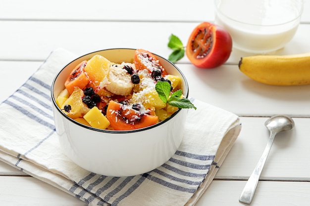 Bowl of fresh fruit salad with coconut flakes and yoghurt in the background