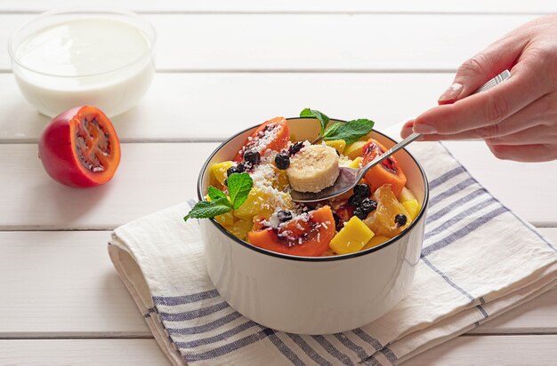 Bowl of fresh fruit salad, with cut tamarillo and yoghurt in the background