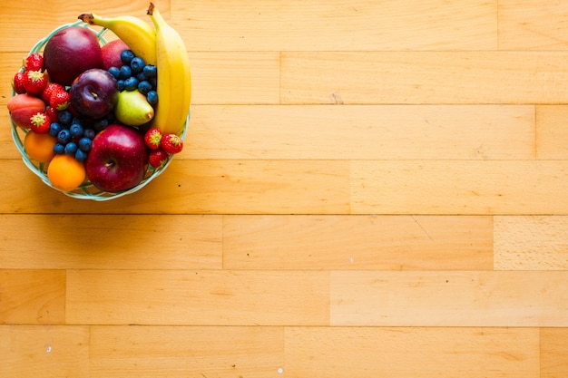 Bowl of fresh fruit with banana apple strawberries apricots blueberries plums whole grains forks top view