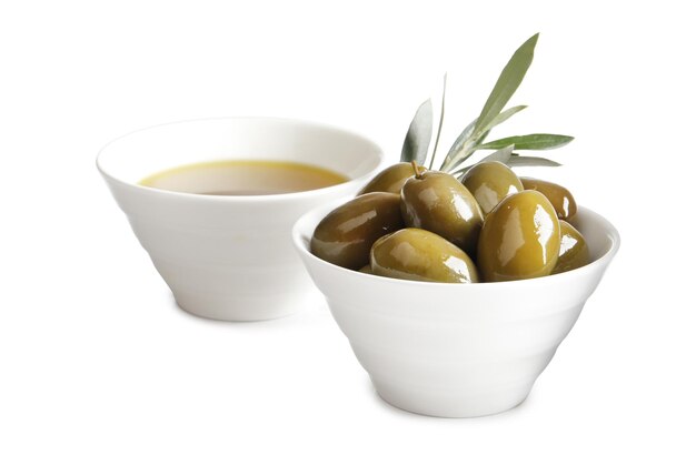 Bowl of fresh olive oil and green olives with leaves isolated on white background. View from above