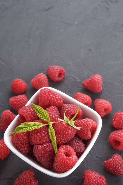 Bowl of fresh raspberries with green leaves on dark beton rock table. Top view.