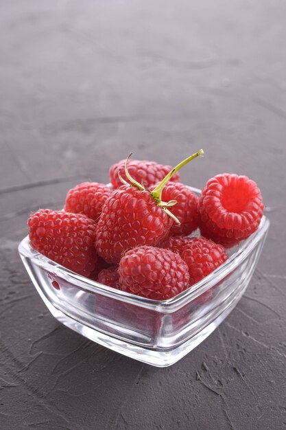 Bowl of fresh raspberries with green leaves on dark rock background.