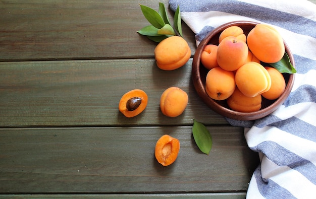 Photo bowl of fresh ripe apricots with leaves on a wooden table