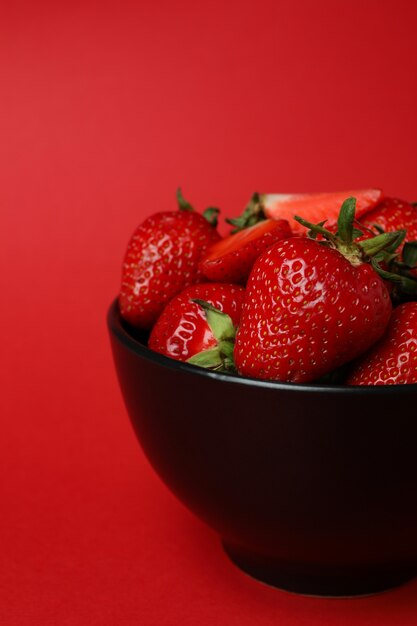 Bowl of fresh strawberry on red surface