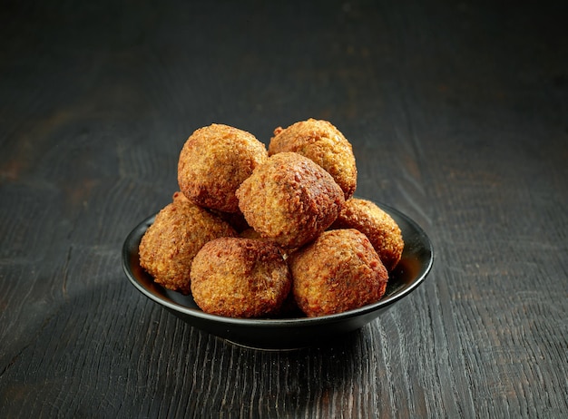 Bowl of fried falafel balls on black wood table