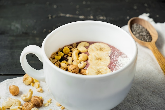 Bowl of fruit smoothie, nuts and banana. Acai bowl with cereals, cashews and hazelnuts on vintage rustic table