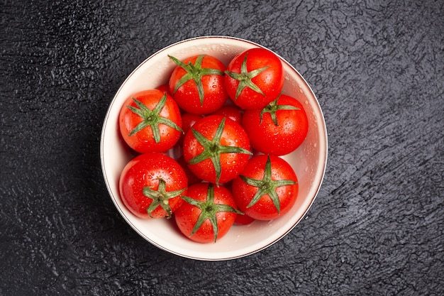 A bowl full of delicious tomatoes on a black table