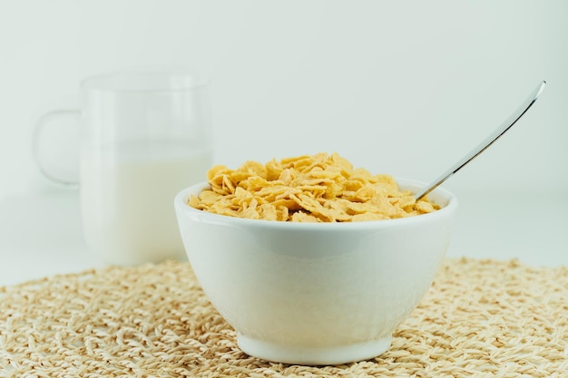 Bowl full of healthy cornflakes and glass of milk with white bottom.