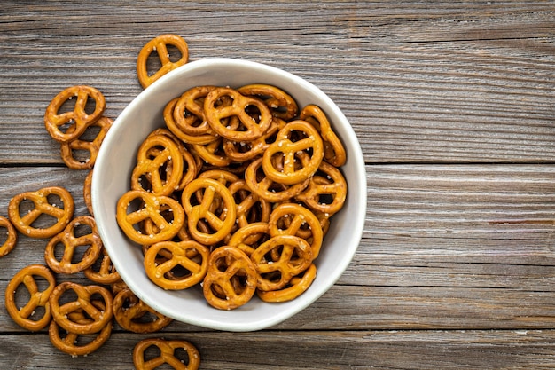 A bowl full of mini pretzels with salt on wooden background top view copy space