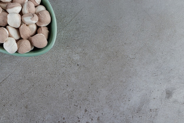 A bowl full of sweet round candies on a stone table. 