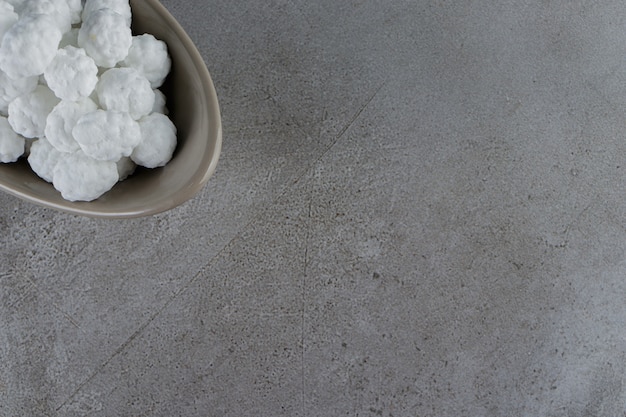 A bowl full of sweet white candies on a stone table . 