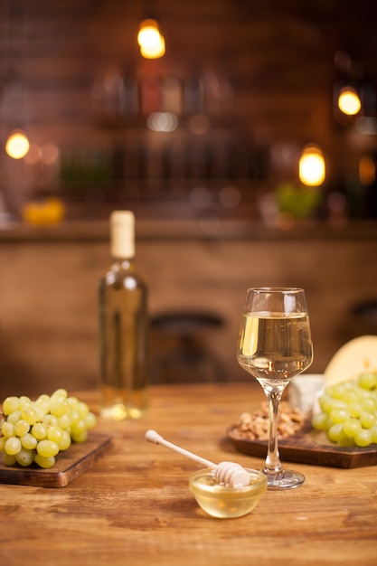 Bowl of golden honey jar next to fresh grapes and wolnuts over a wooden table. Bottle and glass of white wine.