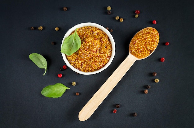 Bowl of grainy mustard and spoon of dijon mustard on black background