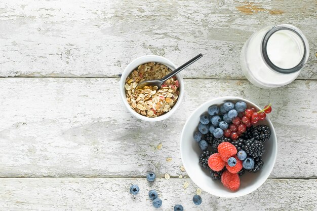 Bowl of granola, milk bottle and bowl of berries on wood