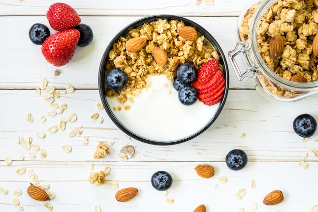 bowl of granola with yogurt, fresh berries, strawberry on wood table.