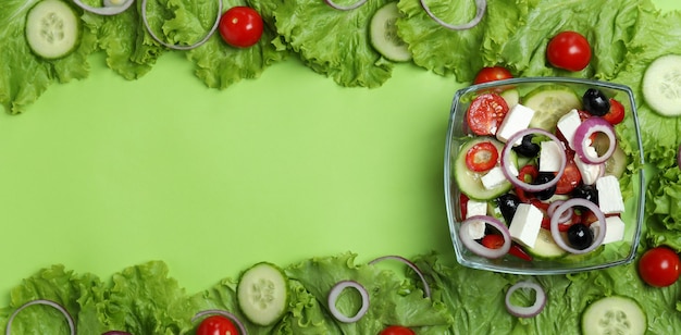 Bowl of greek salad and ingredients on green surface