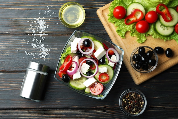 Bowl of greek salad and ingredients on wooden background