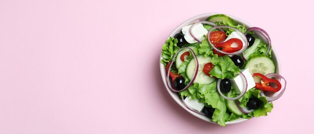 Bowl of greek salad on pink background