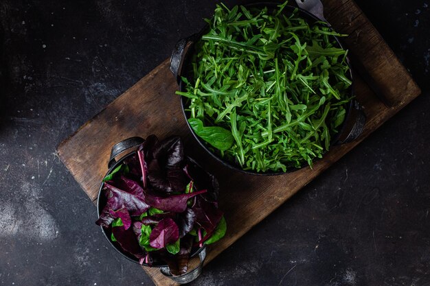 A bowl of green arugula sits on a wooden cutting board next to a bowl of green arugula.