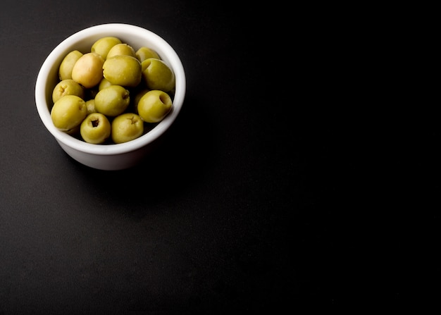 Bowl of green fresh olive over black backdrop
