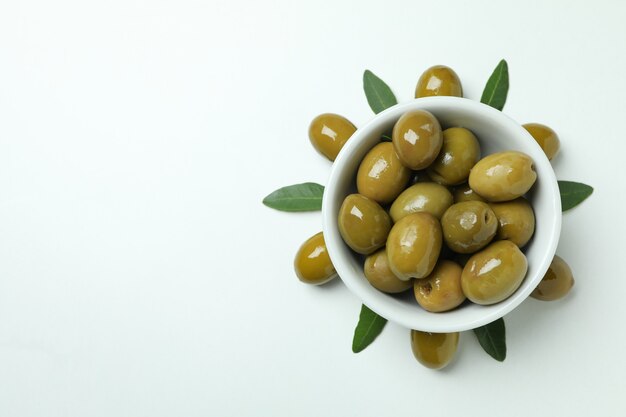 Bowl of green olives and leaves on white background