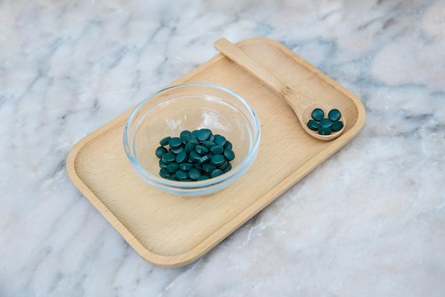 A bowl of green pills on a wooden tray with a spoon on the side.