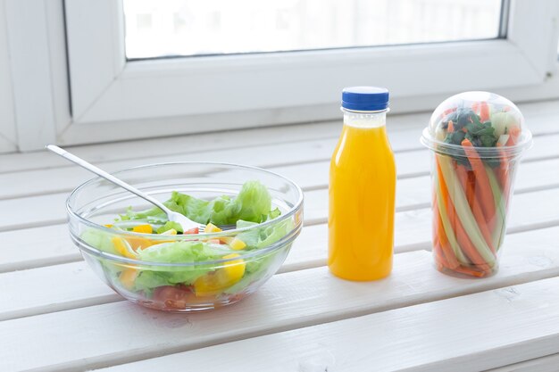 Bowl of green salad, raw vegetables and bottle of orange juice. Weight loss, diet and right