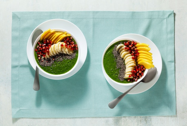 Bowl of green smoothie with sliced mango, banana, pomegranate seeds and chia seeds, maple syrup for a healthy morning breakfast