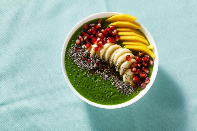 Bowl of green smoothie with sliced mango banana pomegranate seeds and chia seeds maple syrup for a healthy morning breakfast