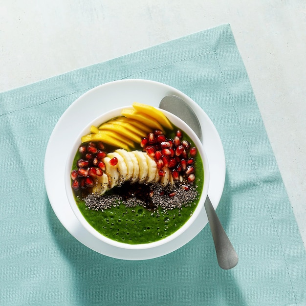 スライスしたマンゴーバナナザクロの種子とチアシードのメープルシロップを添えたグリーンスムージーのボウルで、健康的な朝の朝食をお楽しみください