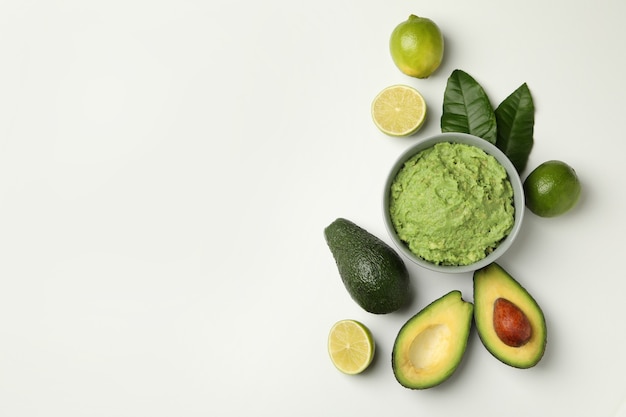 Bowl of guacamole, avocado and lime on white background, space for text