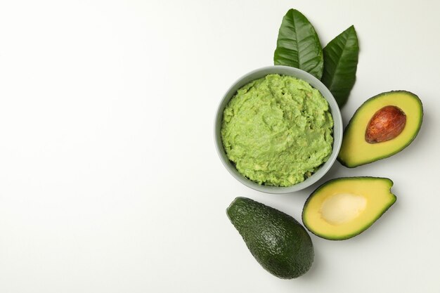 Bowl of guacamole and avocado on white background, space for text