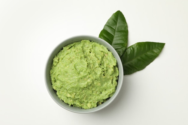 Bowl of guacamole and leaves on white background, top view